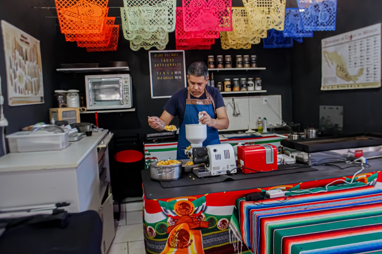 Marco Meléndez, o Chapelão, moendo nixtamal na cozinha artesanal da Testal, decorada com papel picado colorido
